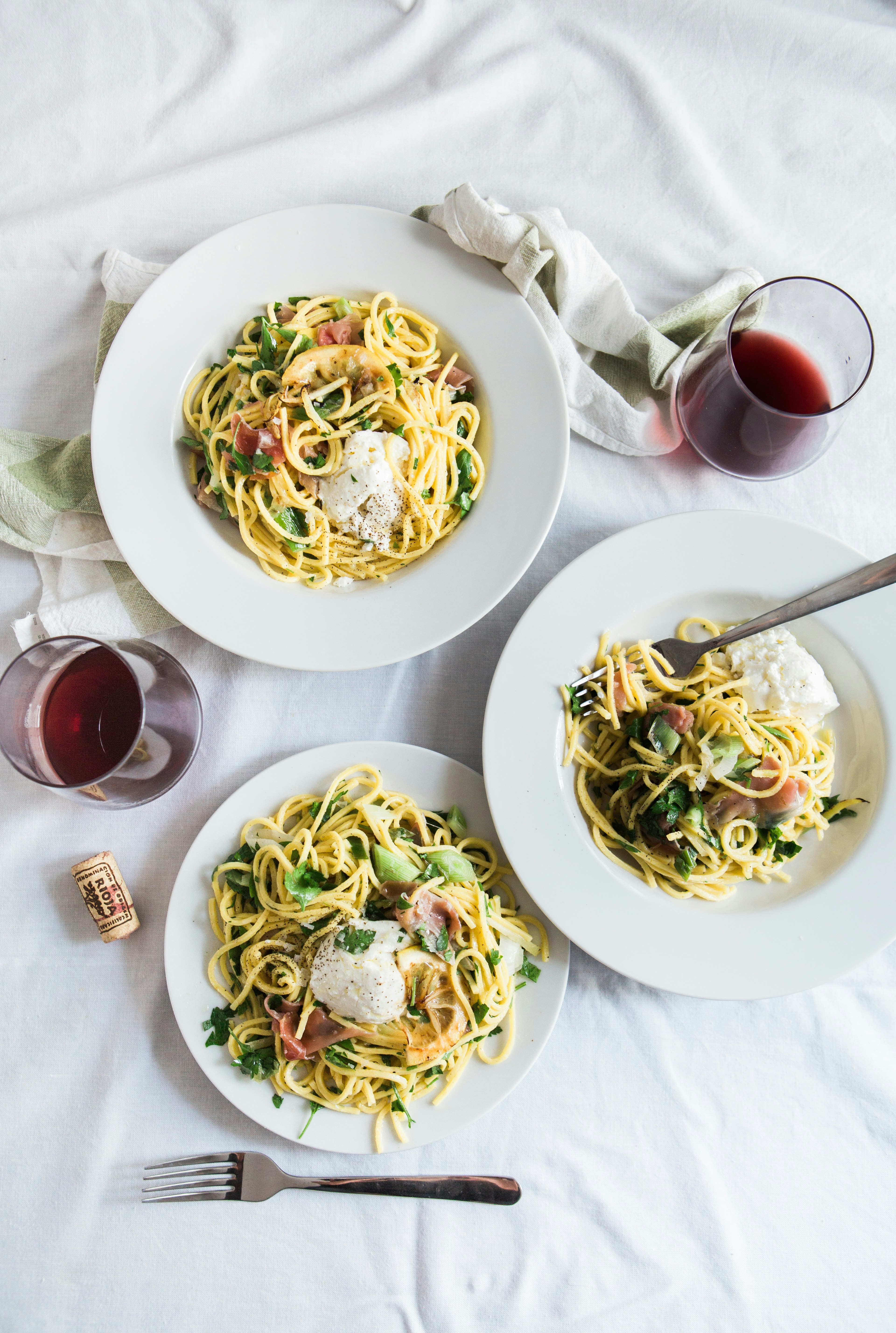 three round white plates with pasta near two glass cuups